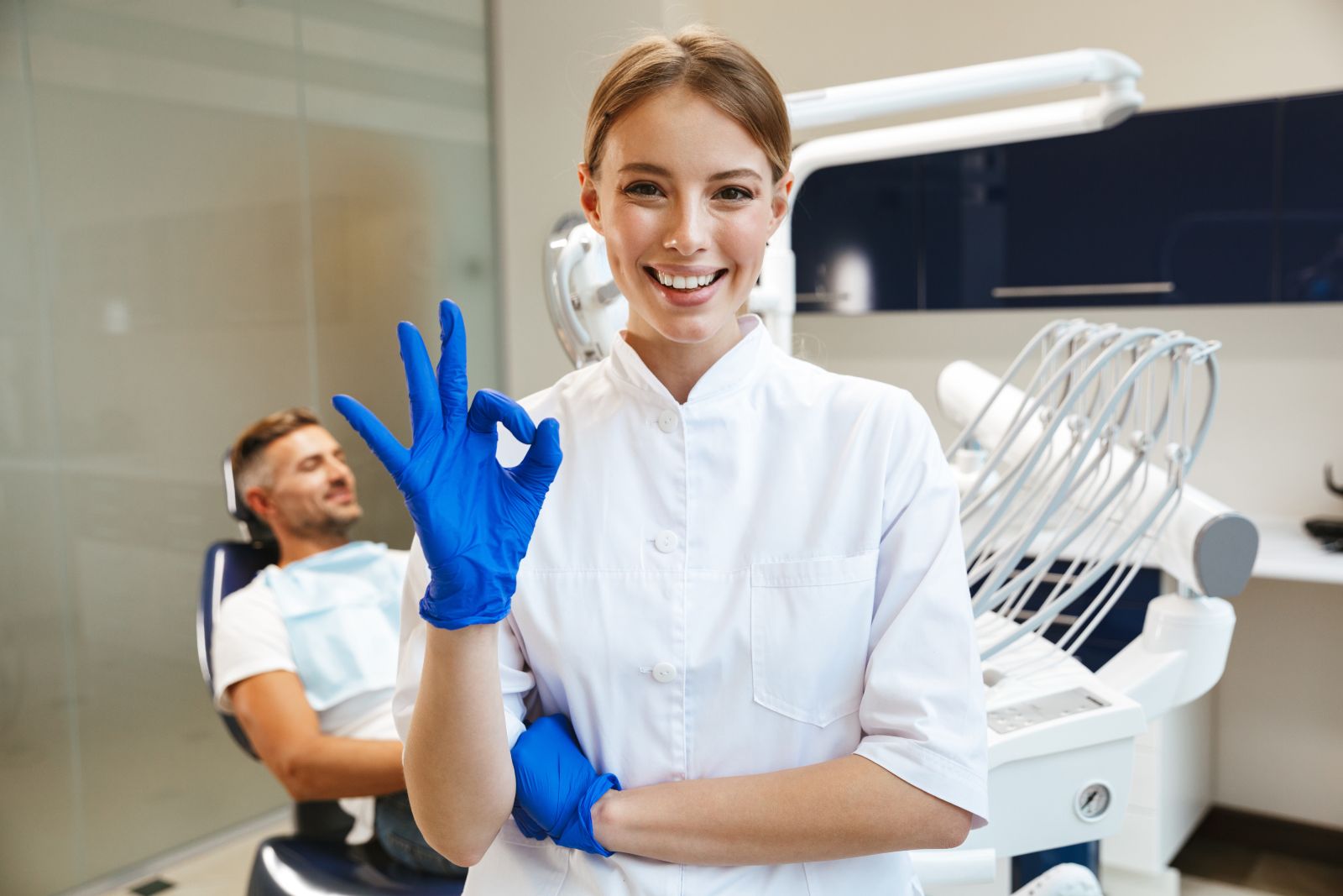 Beautiful happy young woman doctor in medical dentist center showing okay gesture